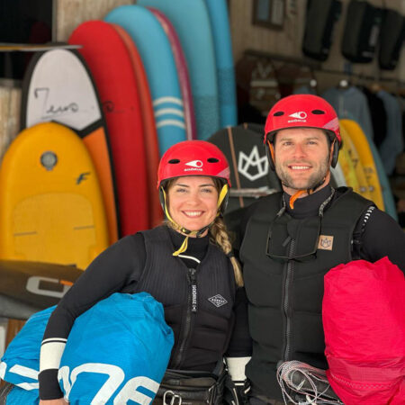 Happy kitesurf student ready in safety helmets for their kite lesson with Loving Surf Kite school with surfboards in the background