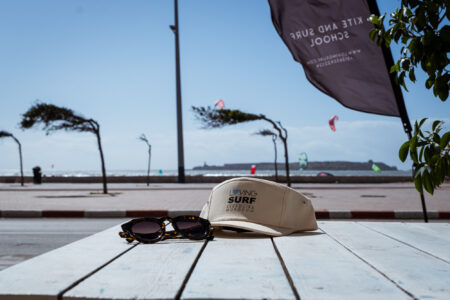 Loving surf hat merch with sunglasses sitting on patio overlooking the beach with kitesurfers riding the waves of Essaouira's bay