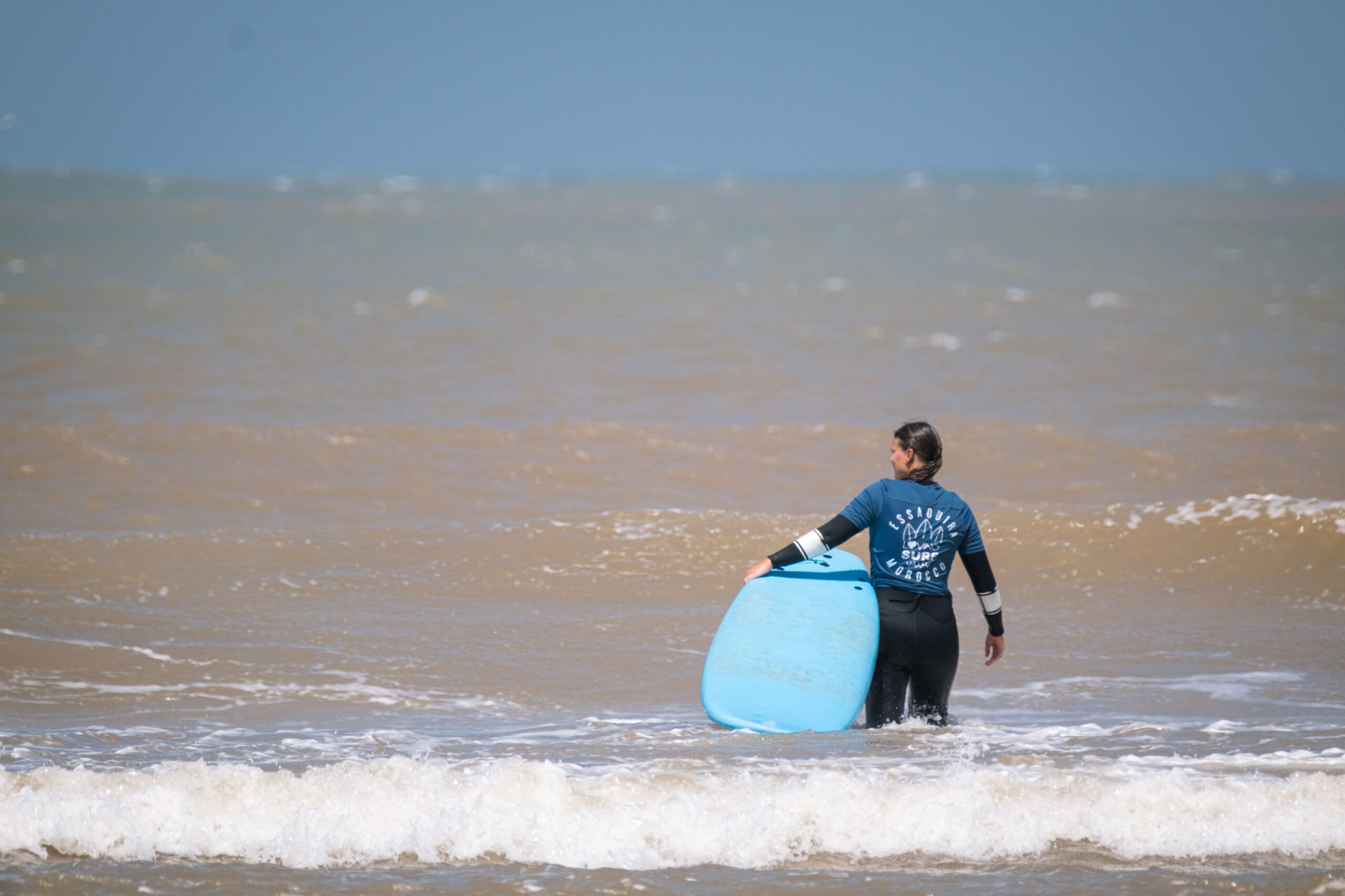 Surfer in loving surf lycra walking out into ocean with surf rental