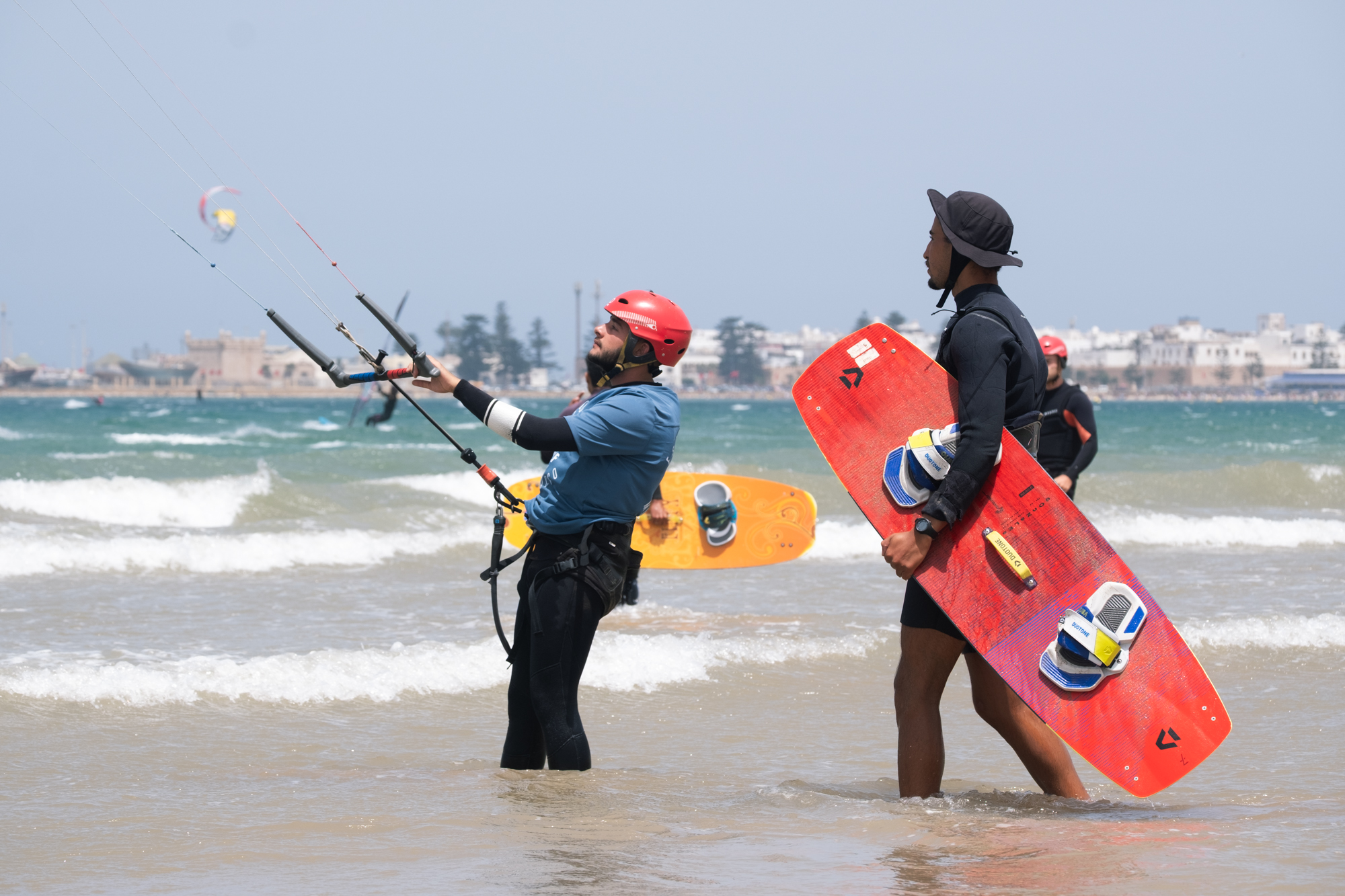 Kitesurf Student heading ou two kite with kite instructor holding the kite board in front of UNESCO old Medina and port of Essaouira Morocco.